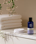 Neal's Yard Remedies' Organic Eye Make Up Remover blue bottom on a granite table besides 2 stacked bath towels.